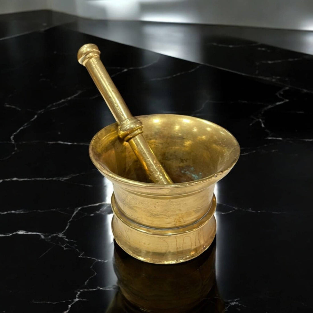 Mortero vintage en bronce con pestillo, estilo tradicional, sobre superficie negra marmoleada. Ideal para decoración clásica de cocina o comedor.