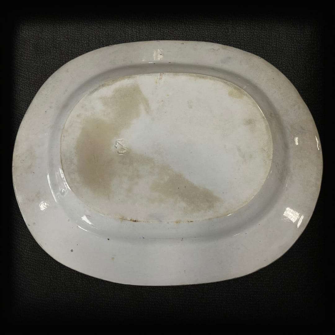 La fuente de loza La Cartuja Pickman es una joya de la cerámica andaluza del siglo XIX, fabricada en la prestigiosa manufactura sevillana La Cartuja de Sevilla, fundada por Charles Pickman. Esta pieza excepcional destaca por su decoración transferware en tono negro sepia, que representa un paisaje orientalista con figuras, arquitectura clásica y ornamentación floral, todo enmarcado por un delicado borde decorado con motivos vegetales.

Con su estilo refinado y su impecable conservación, esta fuente de loza 