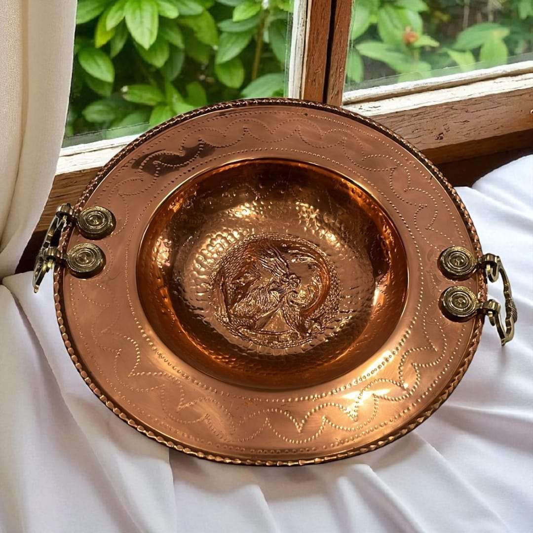 Brasero de cobre artesanal con relieve griego y asas laterales.
