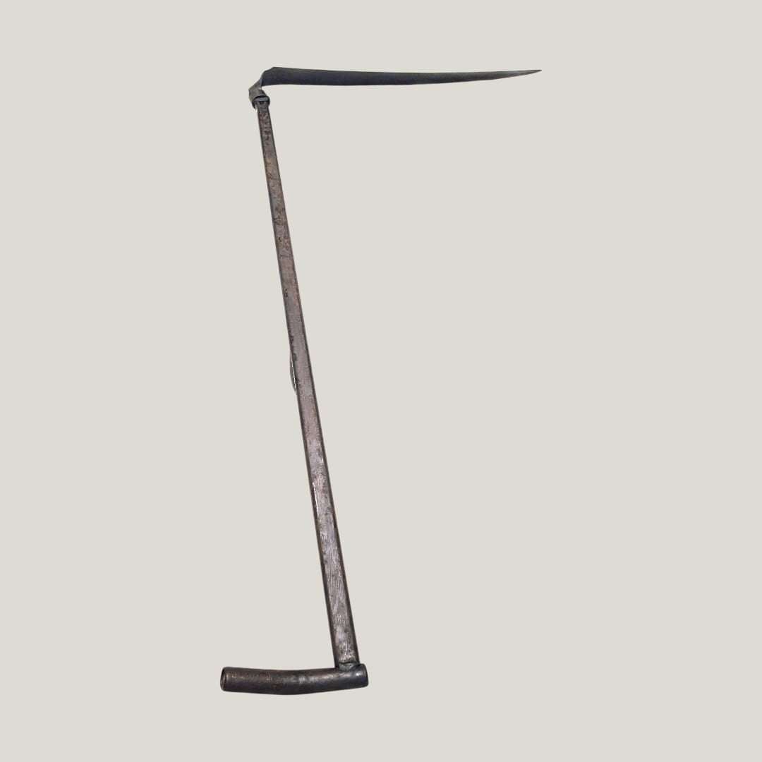 Guadaña antigua decorativa de hierro forjado vista en ángulo, ideal para decoración rústica en espacios de estilo vintage o campestre.