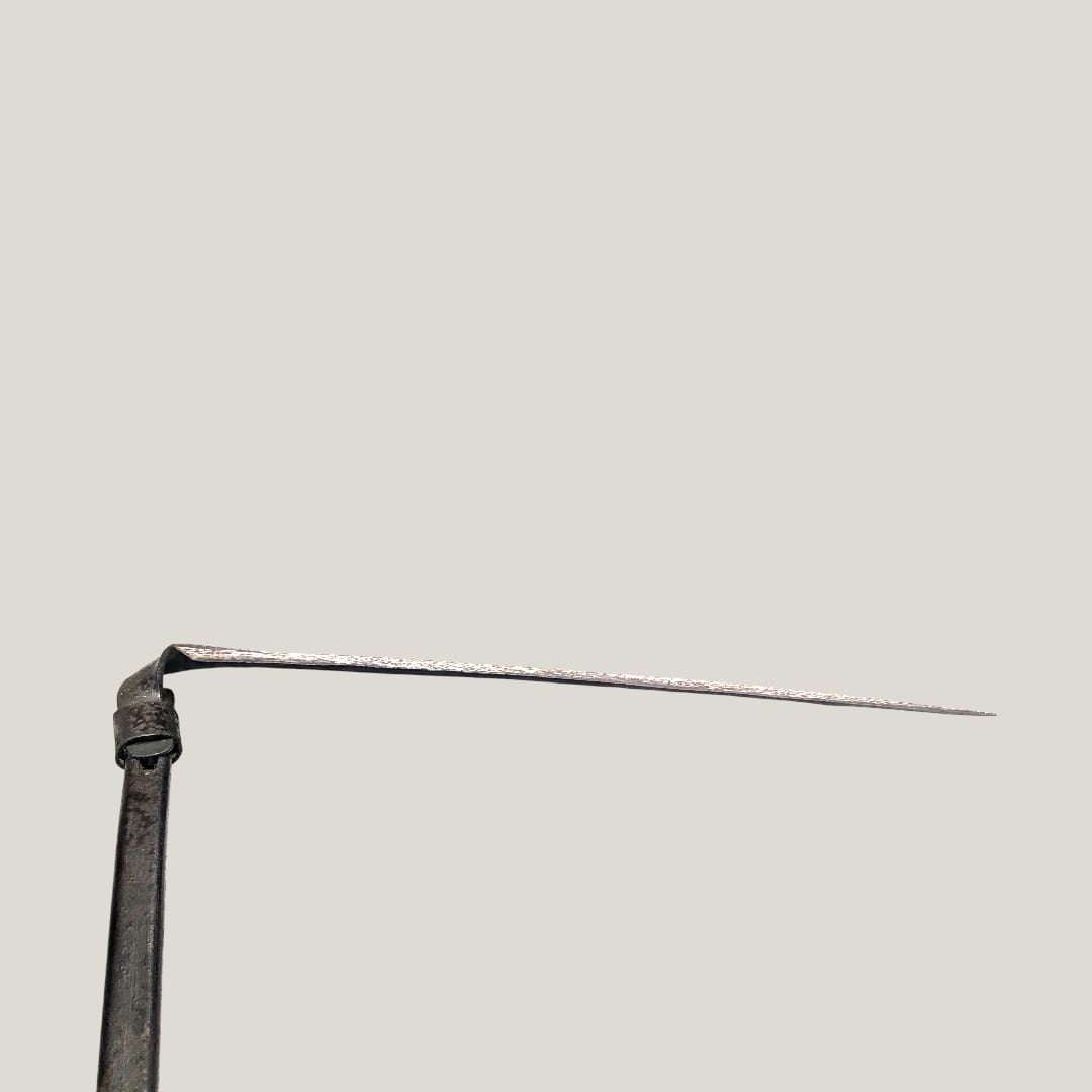 Detalle lateral de la hoja afilada de la guadaña antigua decorativa de hierro forjado, pieza única de inspiración agrícola tradicional.