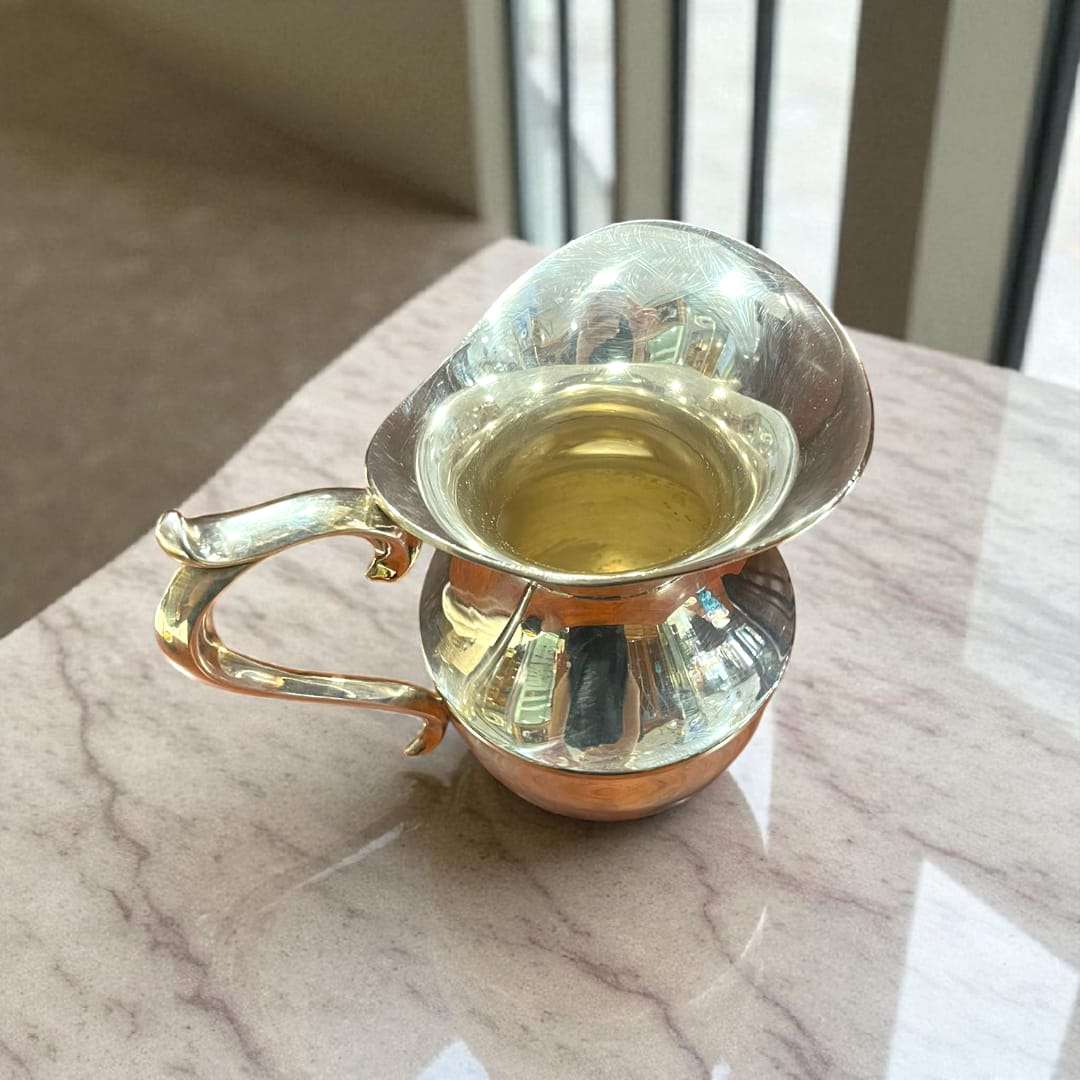 Jarra de metal plateado con asa curva en primer plano.