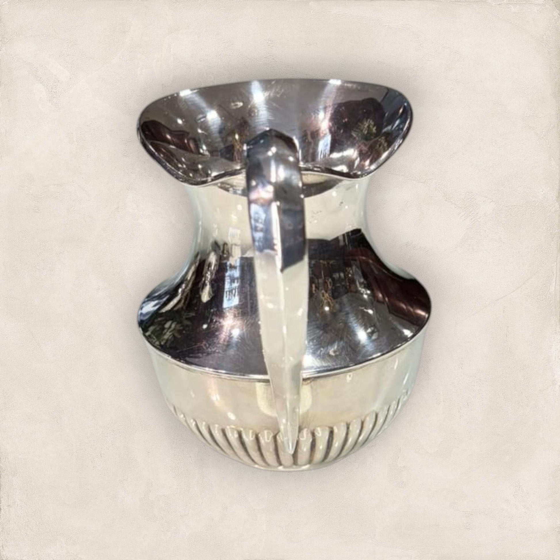 Jarra de metal plateado vista trasera con asa ergonómica, estilo clásico que aporta elegancia y brillo a la decoración del hogar.