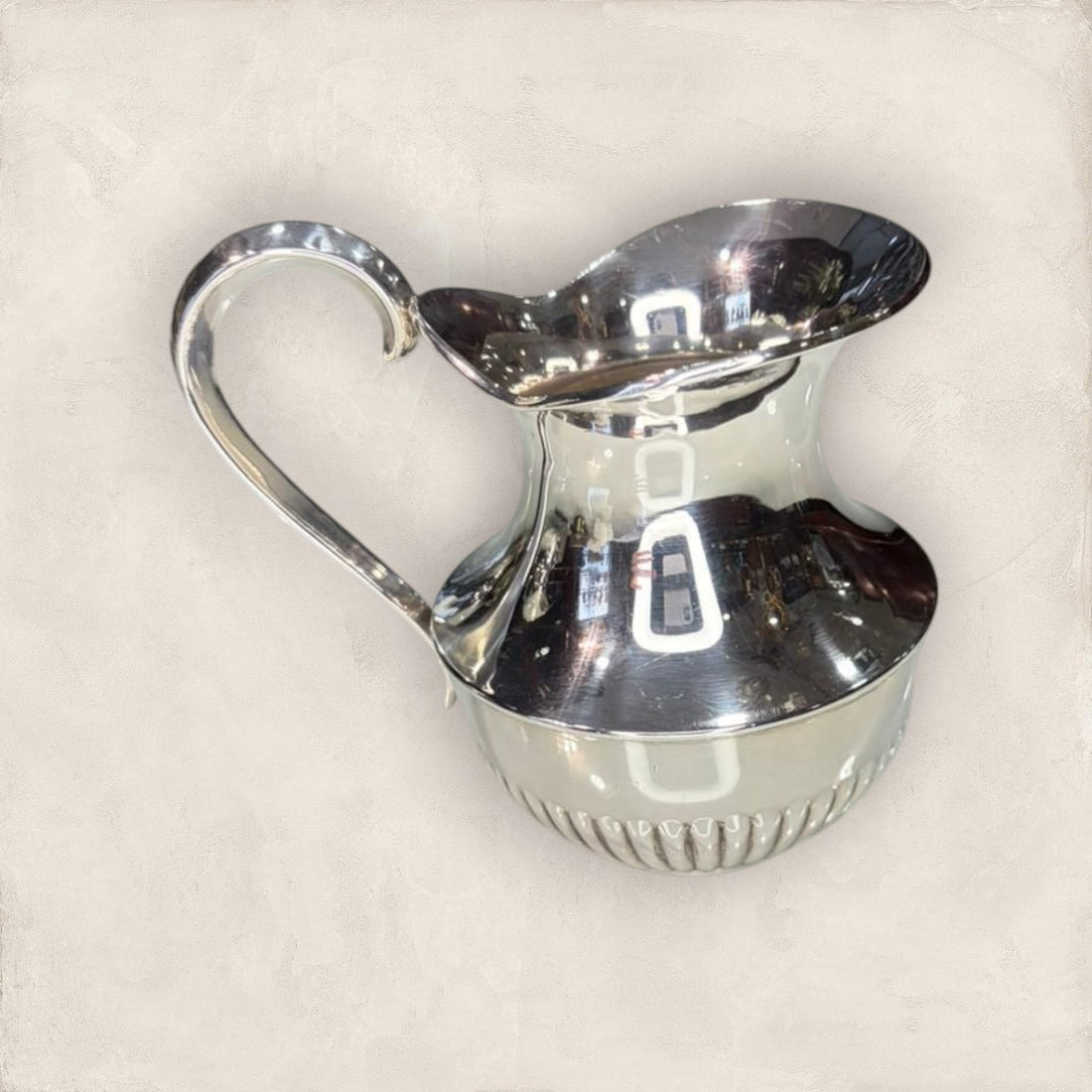 Jarra de metal plateado con acabado brillante y diseño curvo, ideal para decoración elegante en espacios del hogar.