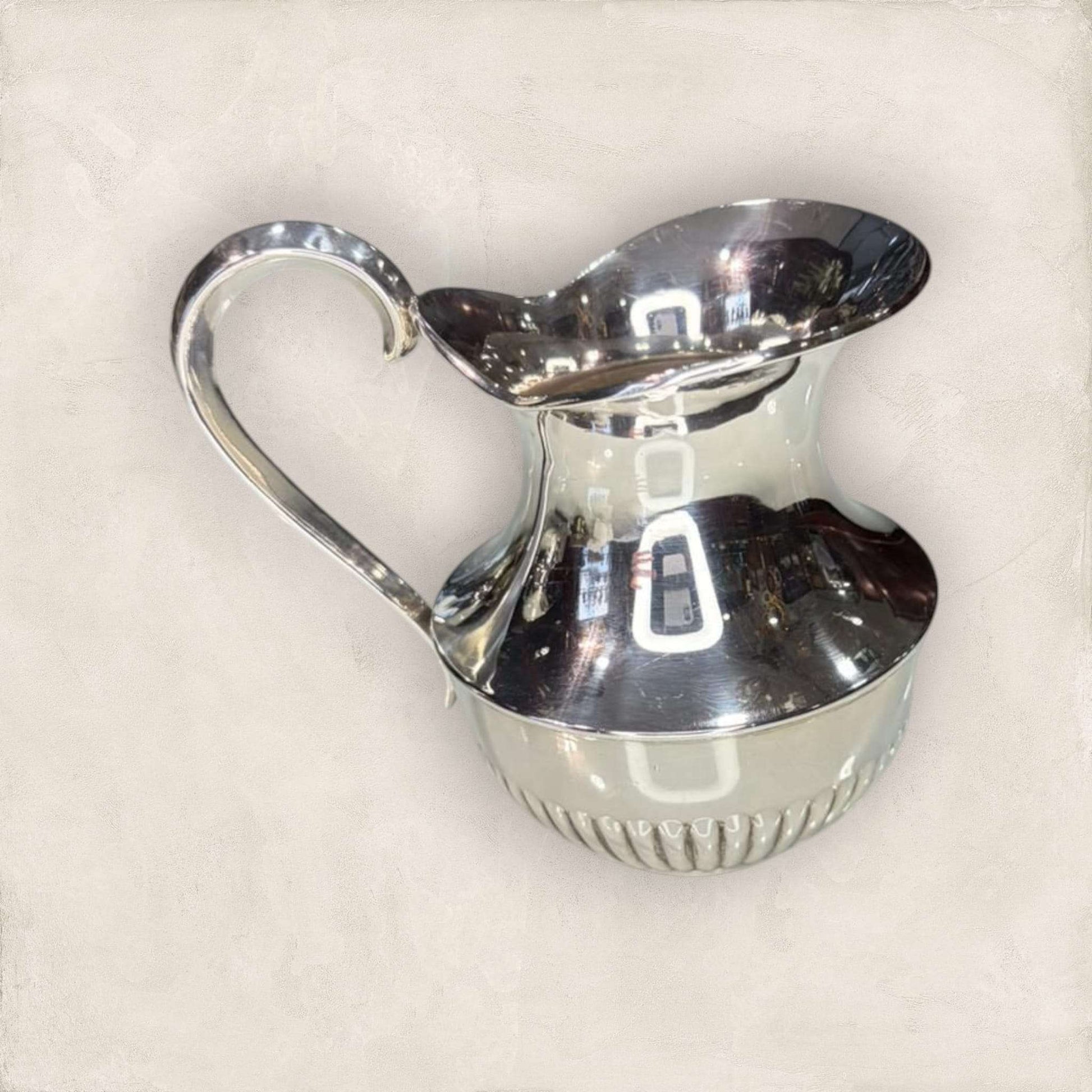 Jarra de metal plateado con acabado brillante y diseño curvo, ideal para decoración elegante en espacios del hogar.