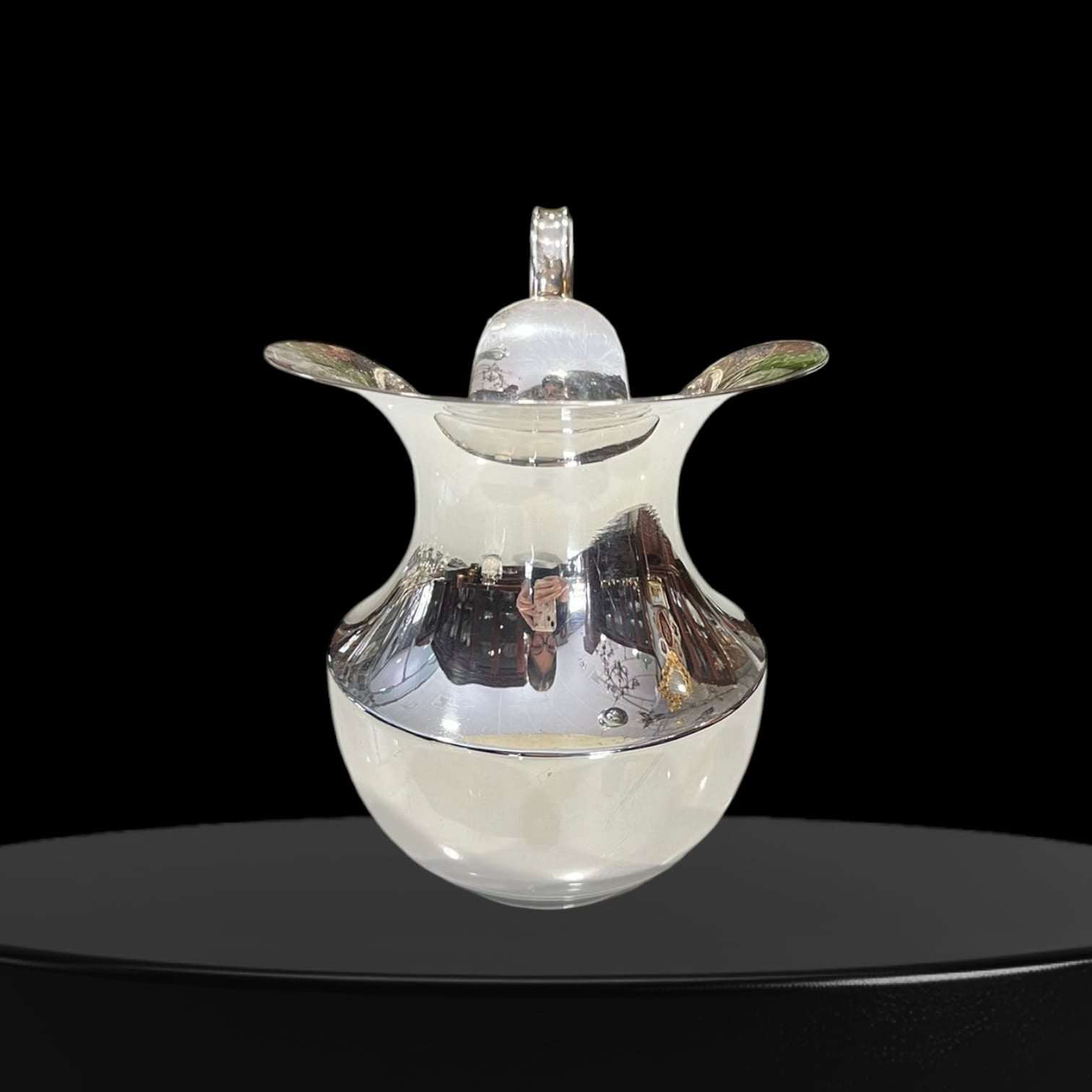 La Jarra de metal plateado cuenta con un acabado brillante tipo espejo que refleja la luz y realza su presencia en cualquier espacio. Además, su asa estilizada y su b