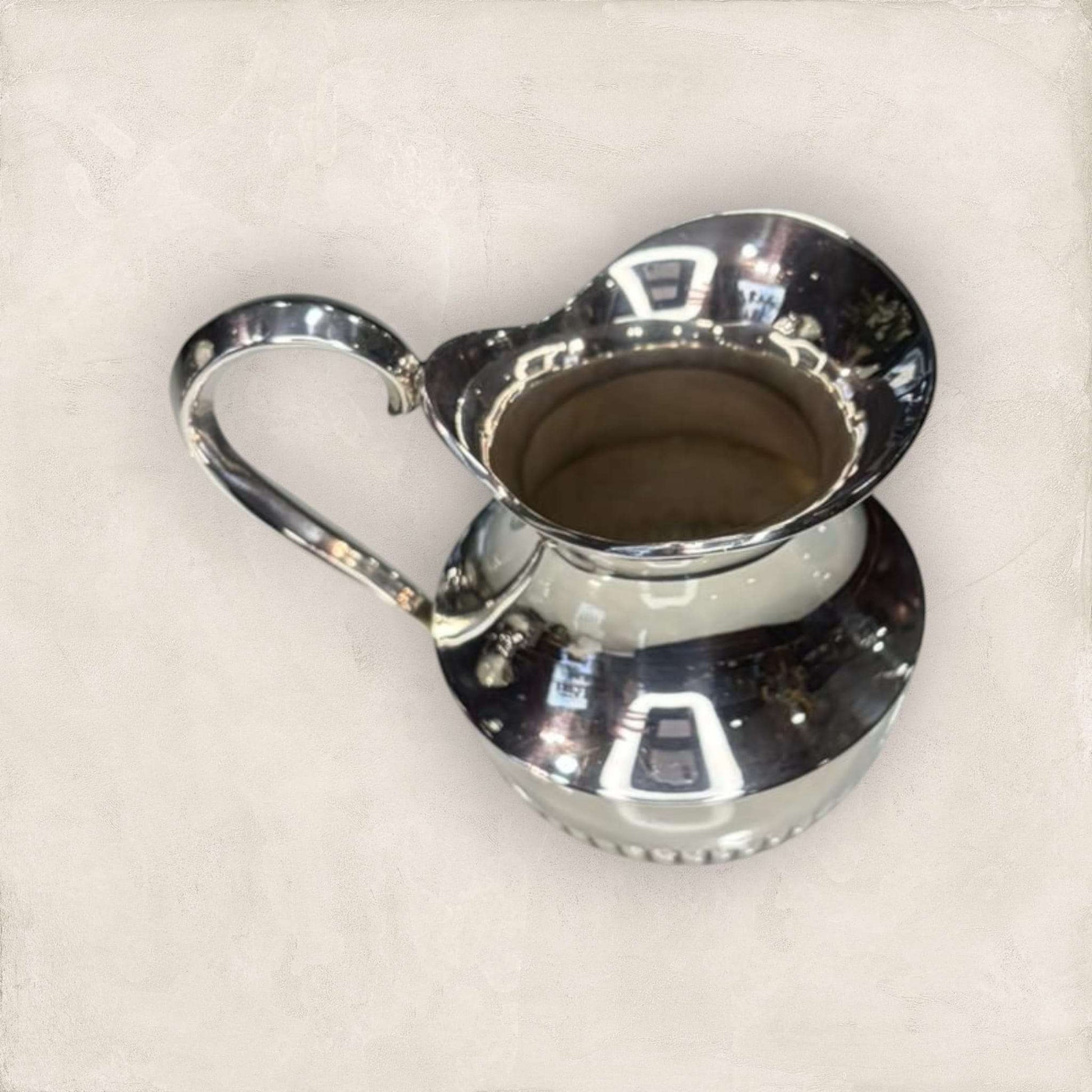 Jarra decorativa de metal plateado con diseño curvado y acabado reflectante, ideal para embellecer espacios interiores.