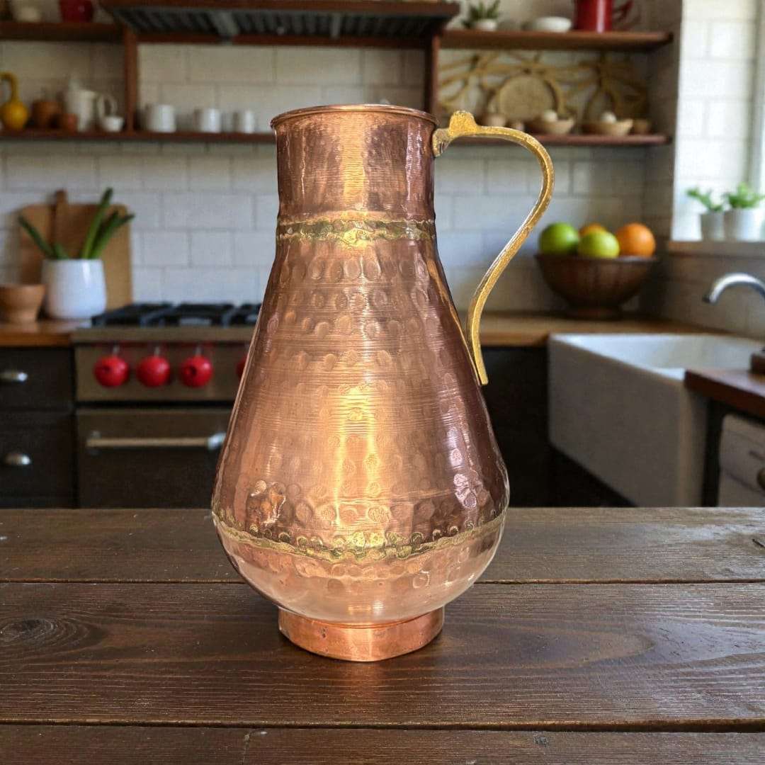 Esta jarra de cobre con asa de metal es una pieza antigua de gran presencia decorativa, elaborada artesanalmente en cobre martilleado, siguiendo técnicas tradicionales. 