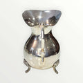 Jarra de metal plateado con diseño intemporal y patas decorativas, ideal para decoración elegante en el hogar. Elegancia clásica para interiores.