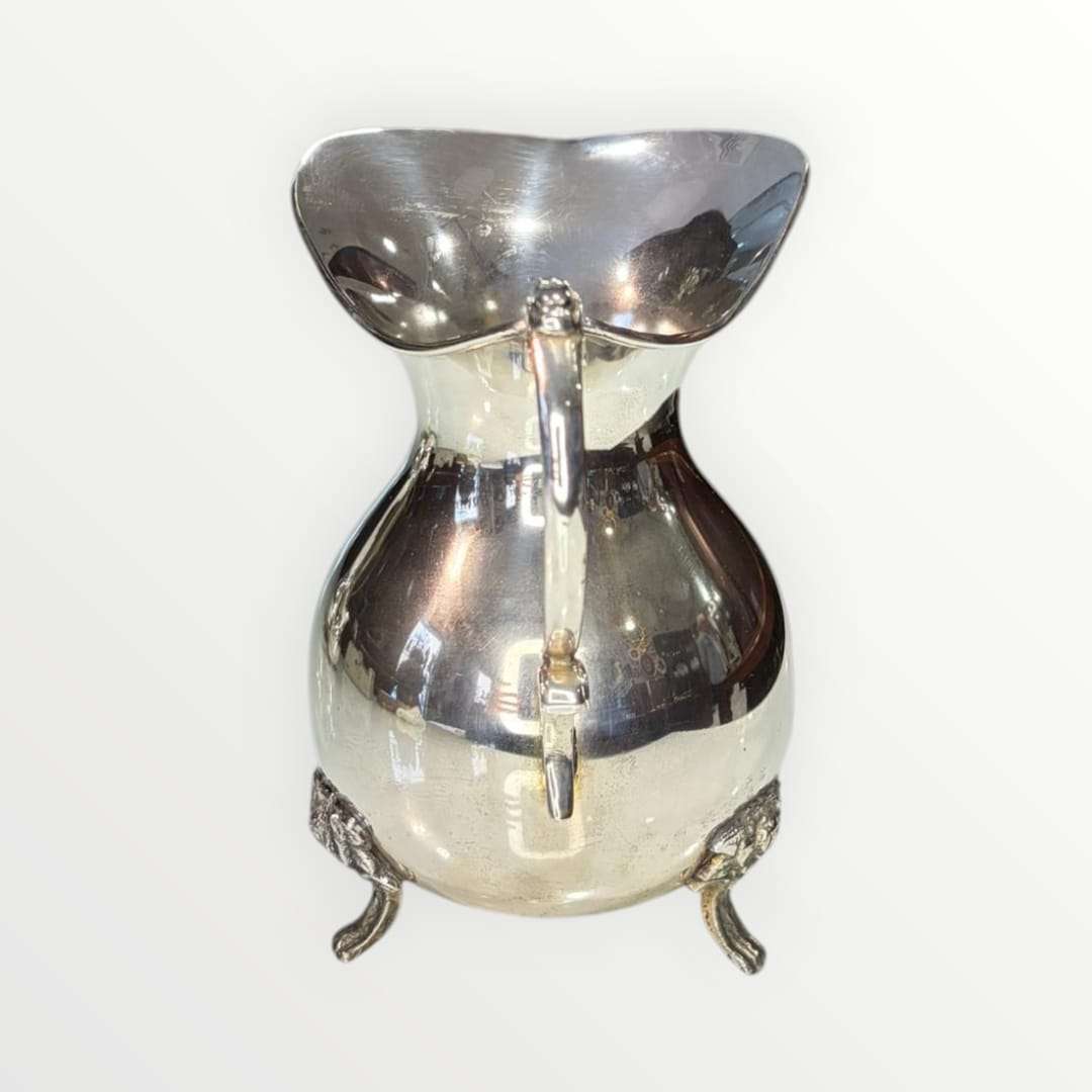 Jarra de metal plateado con diseño intemporal y patas decorativas, ideal para decoración elegante en el hogar. Elegancia clásica para interiores.