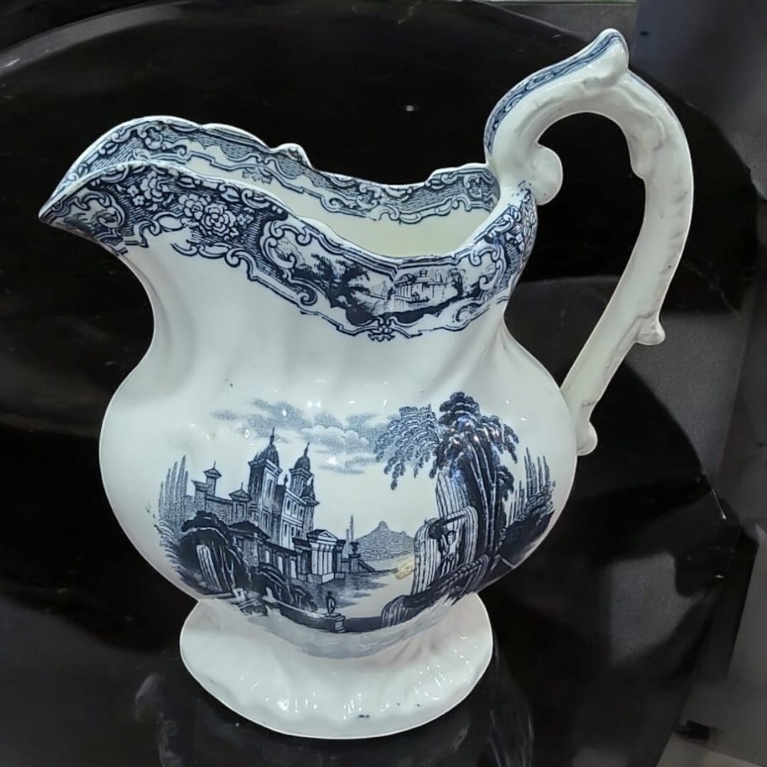 Jarra de Pickman con diseño vintage en cerámica blanca y azul, decorada con escenas clásicas. Pieza exclusiva para decoración y colección.