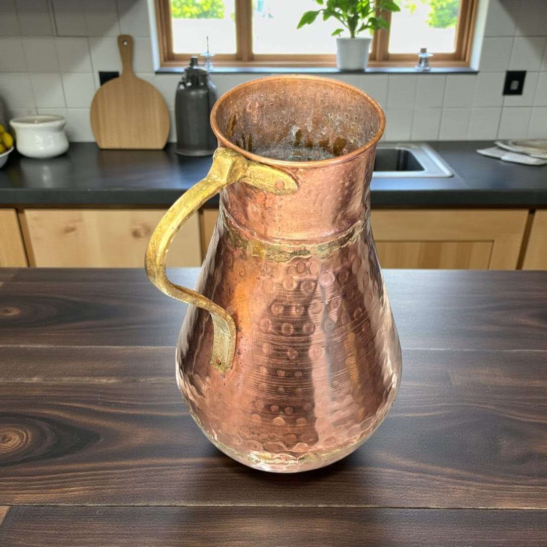 Esta jarra de cobre con asa de metal es una pieza antigua de gran presencia decorativa, elaborada artesanalmente en cobre martilleado, siguiendo técnicas tradicionales. 