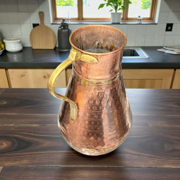 Esta jarra de cobre con asa de metal es una pieza antigua de gran presencia decorativa, elaborada artesanalmente en cobre martilleado, siguiendo técnicas tradicionales. 