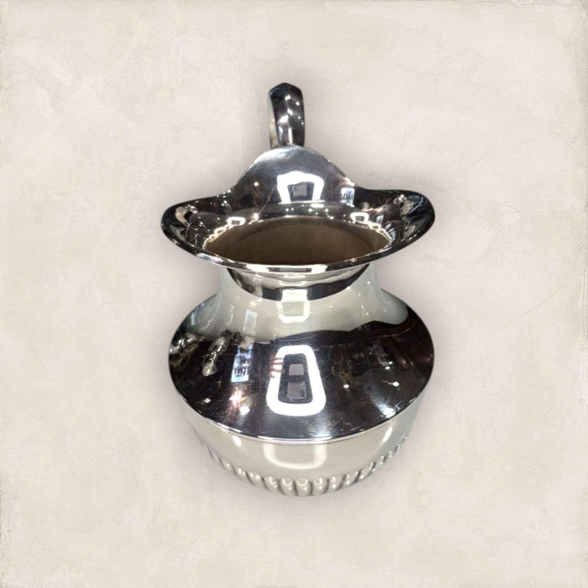 Jarra de metal plateado con base acanalada y forma elegante, perfecta para decoración de interiores en estilo clásico y funcional.