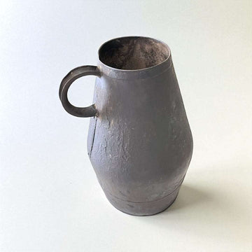 Jarra de trasiego antigua en metal con acabado envejecido, ideal como decoración vinícola rústica para el hogar o jardín.