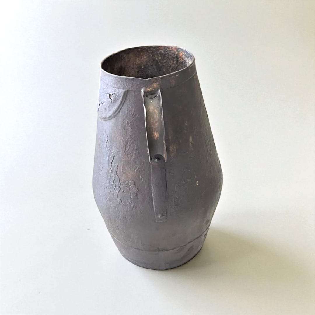 Jarra de trasiego antigua en metal con acabado envejecido, ideal como decoración vinícola rústica para el hogar o jardín.