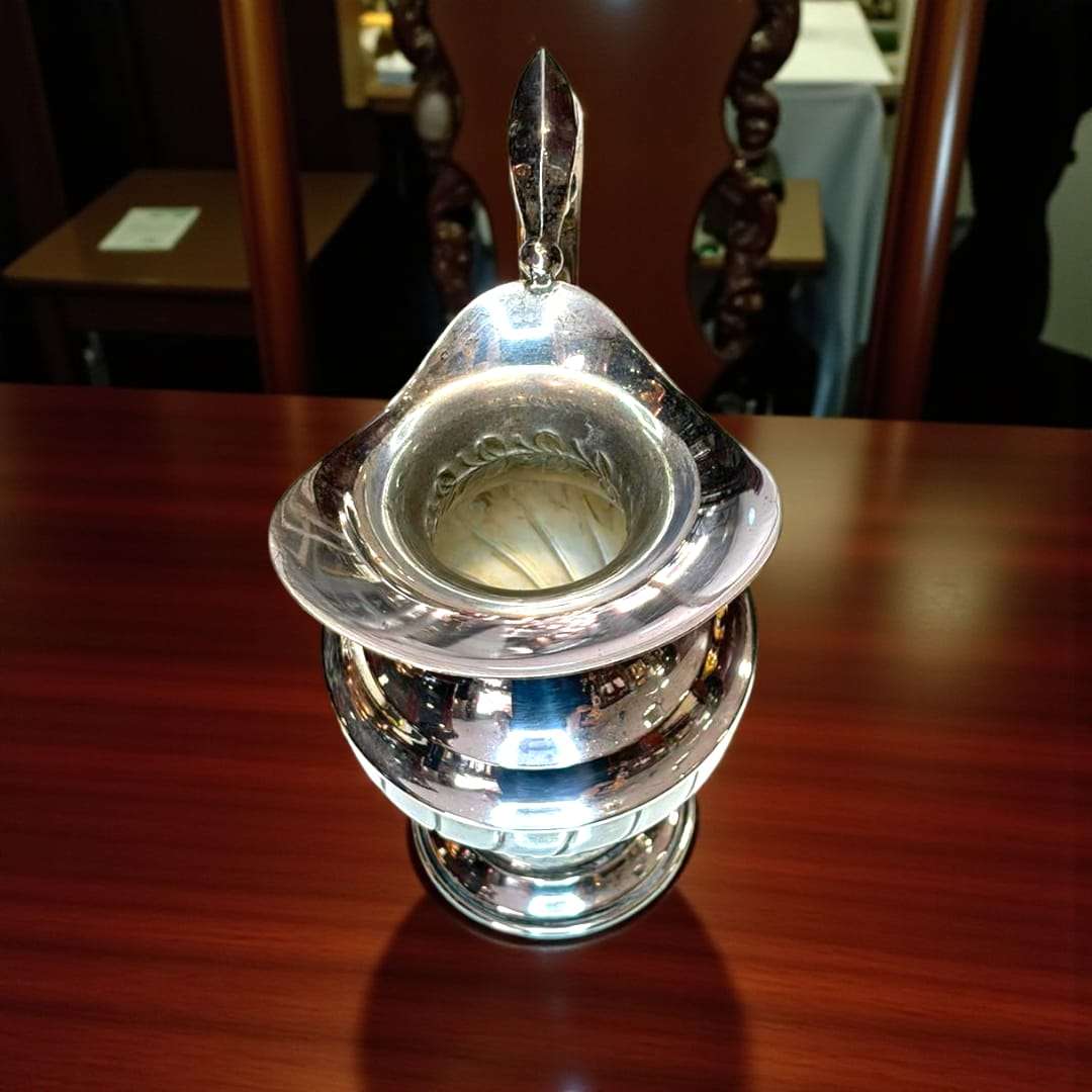 Jarra de metal plateado con brillo pulido sobre mesa de madera.