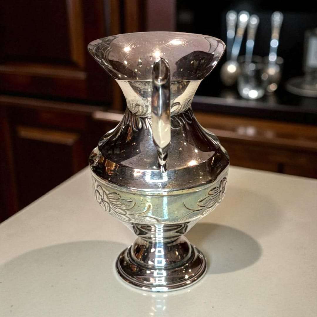 Jarra de metal plateado con brillo pulido sobre mesa de madera.