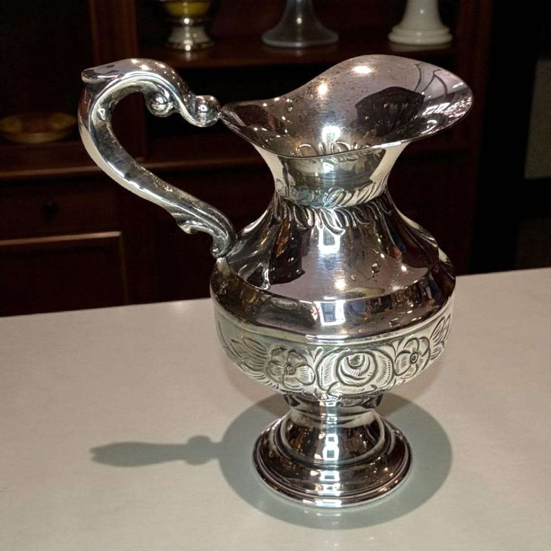 Jarra de metal plateado con brillo pulido sobre mesa de madera.