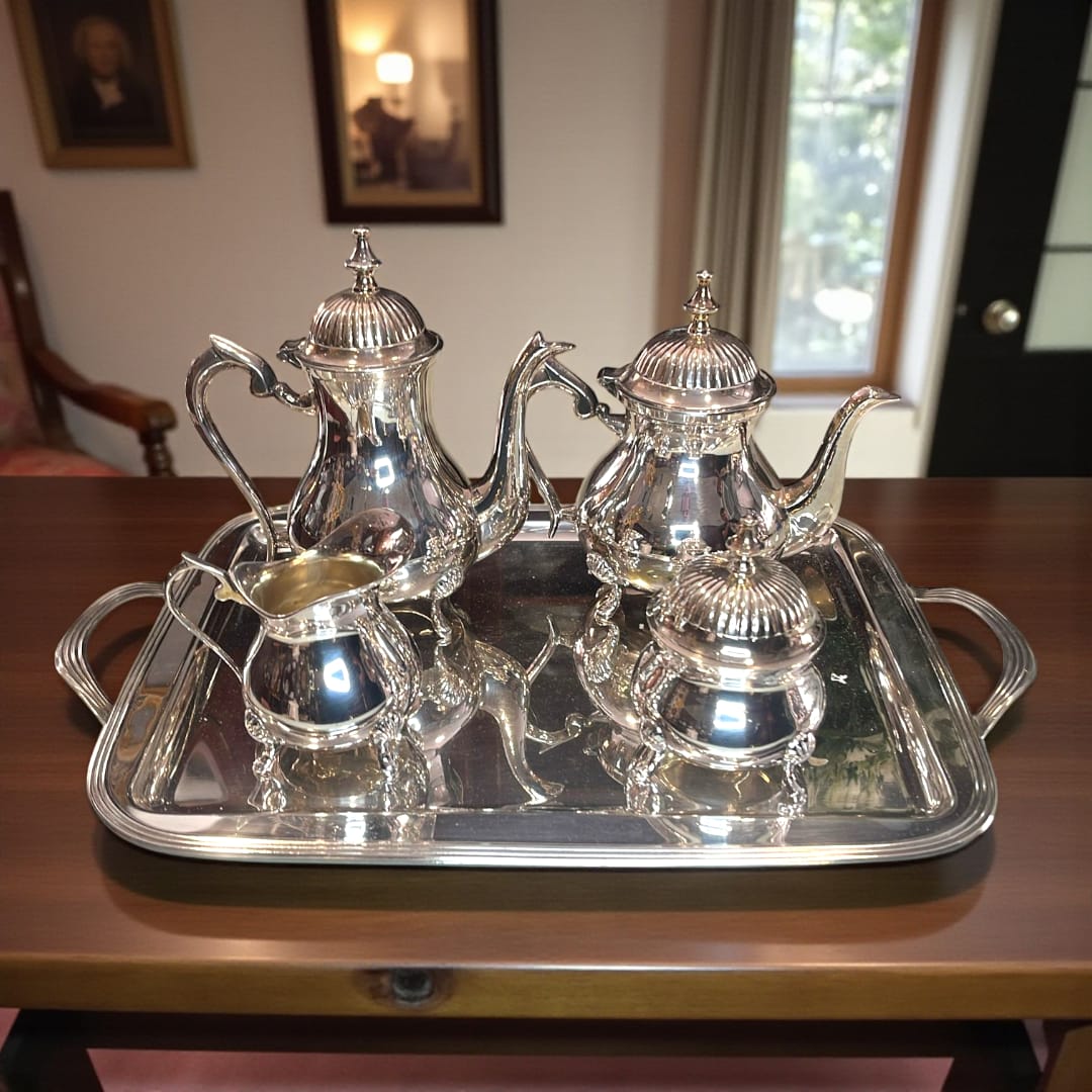 Juego de café plateado completo sobre bandeja reflejante junto a una ventana.