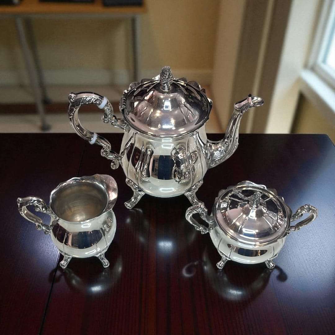 Conjunto de piezas de café de metal plateado sobre mesa oscura.