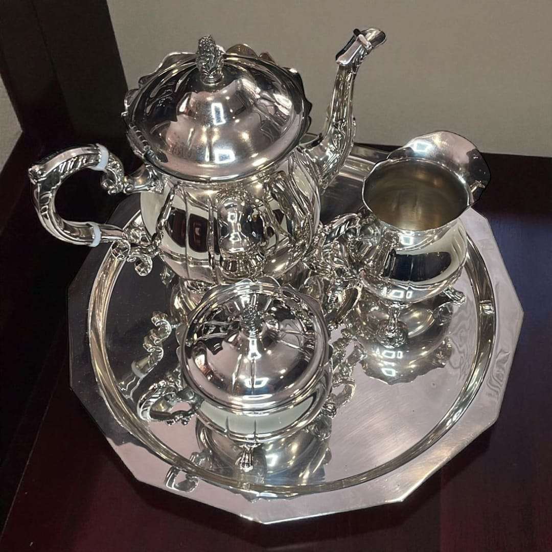 Conjunto de café de metal plateado reflejando la luz en bandeja pulida.