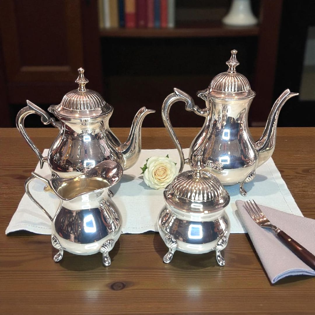 Juego de café plateado completo sobre bandeja reflejante junto a una ventana.