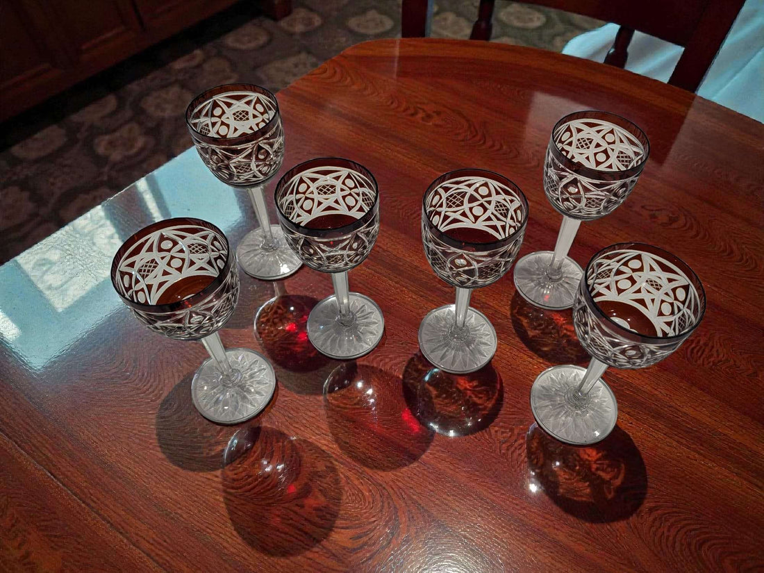 Juego de licorera con 6 copas de cristal tallado con color ámbar y rojo, sobre mesa de madera, ideal para decoración elegante de interiores.