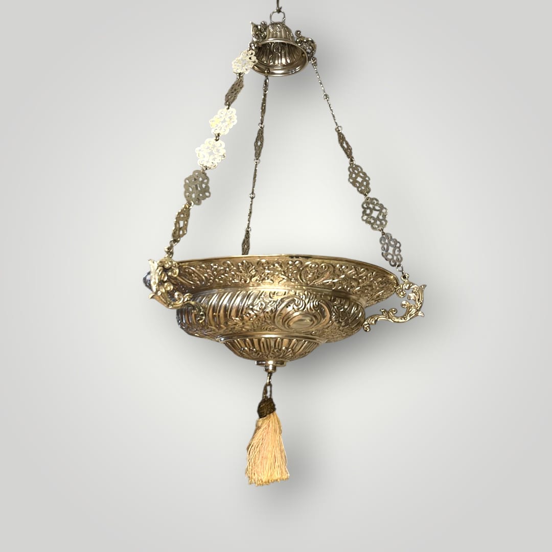 Lámpara votiva de metal plateado colgante con borla dorada.