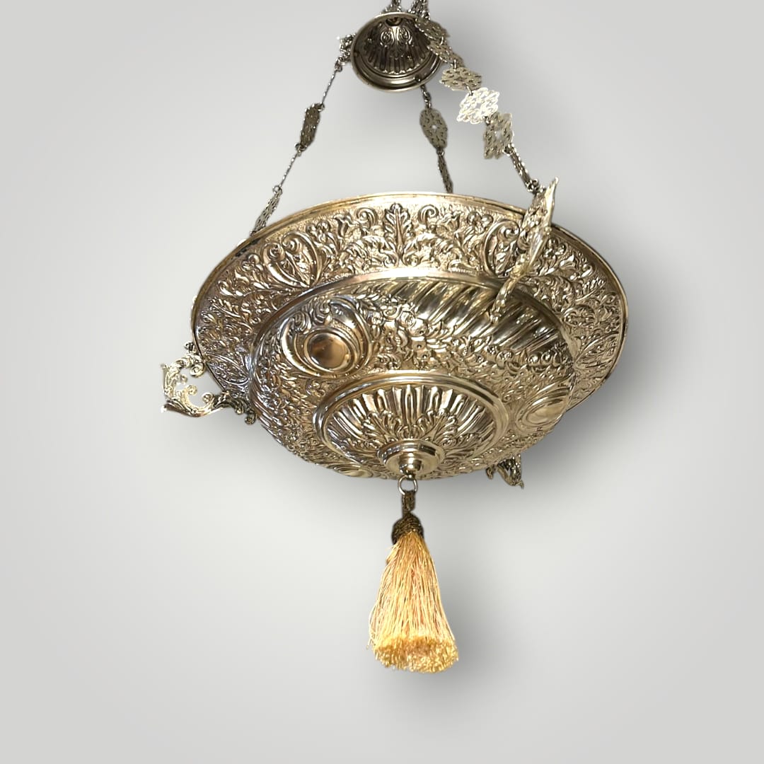 Lámpara votiva de metal plateado colgante con borla dorada.