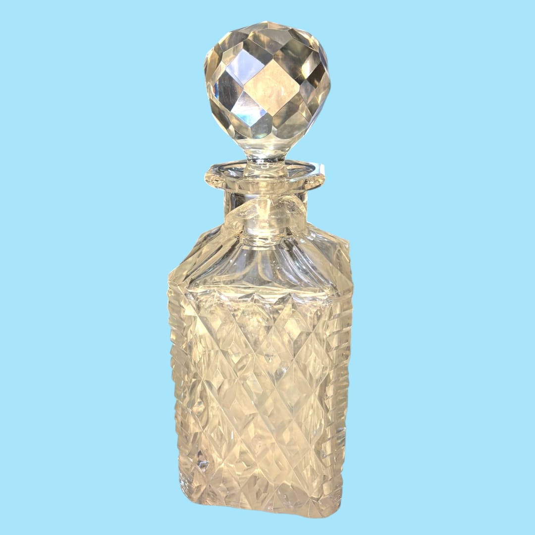 Licorera de cristal con cuello de plata, diseño tallado en patrón de diamante y tapón facetado. Elegancia decorativa para el hogar o colección.