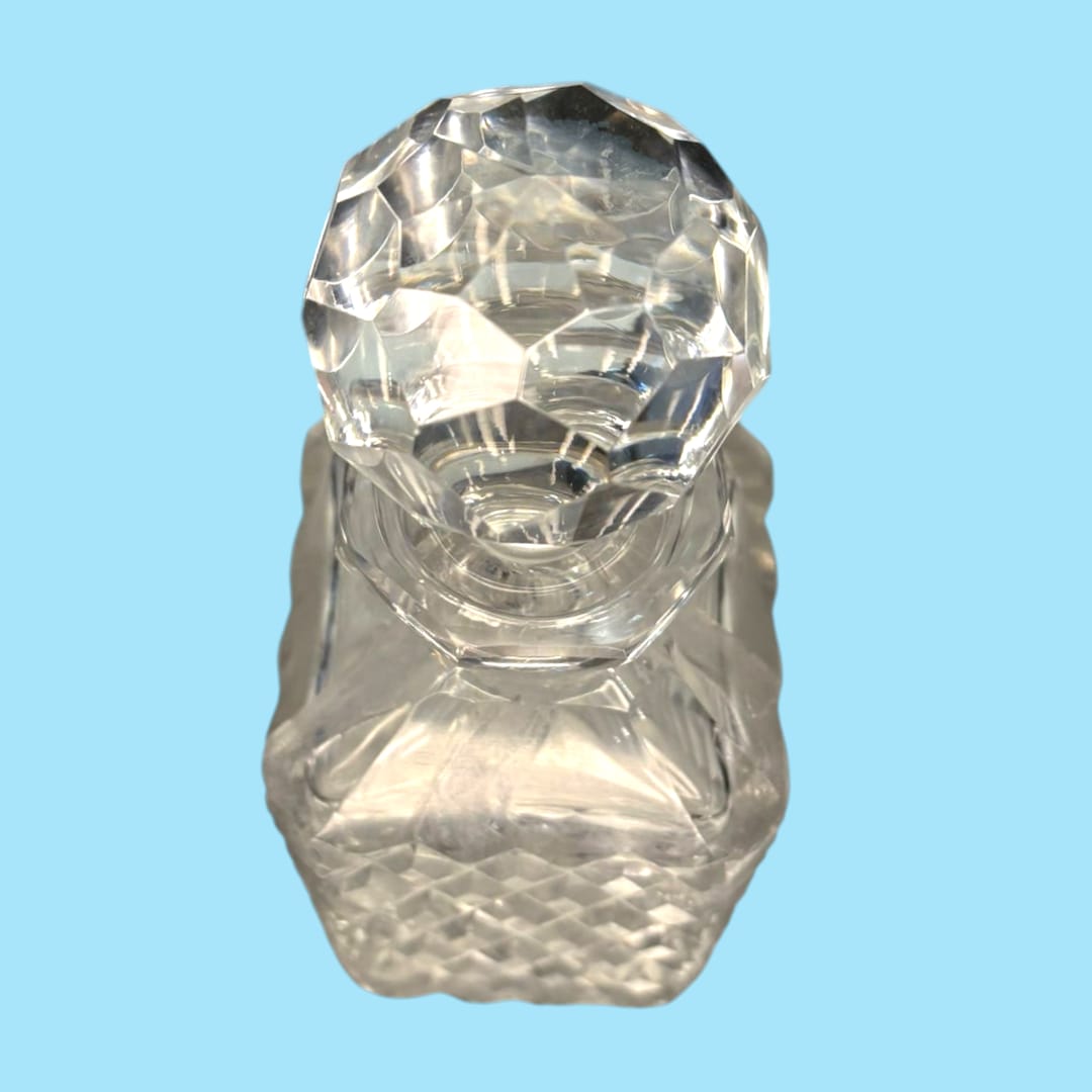 Licorera de cristal con cuello de plata, diseño tallado en patrón de diamante y tapón facetado. Elegancia decorativa para el hogar o colección.
