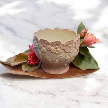 Maceta cerámica rosa esmaltada con relieve floral único sobre bandeja de madera decorada con flores, ideal para decoración de interiores elegantes.