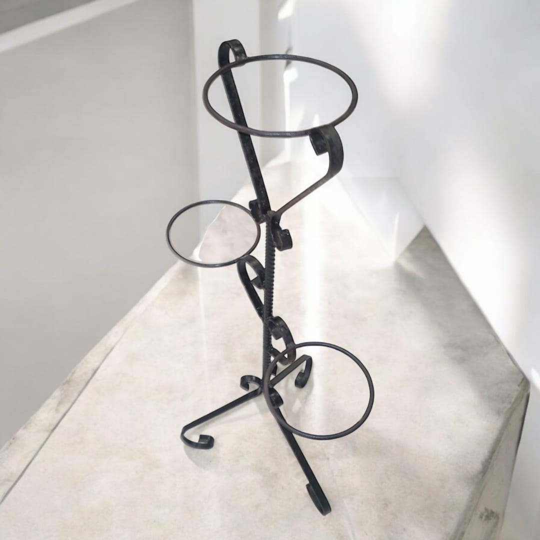 Macetero de 3 soportes en perspectiva lateral, resaltando el diseño clásico con volutas decorativas y estructura firme.