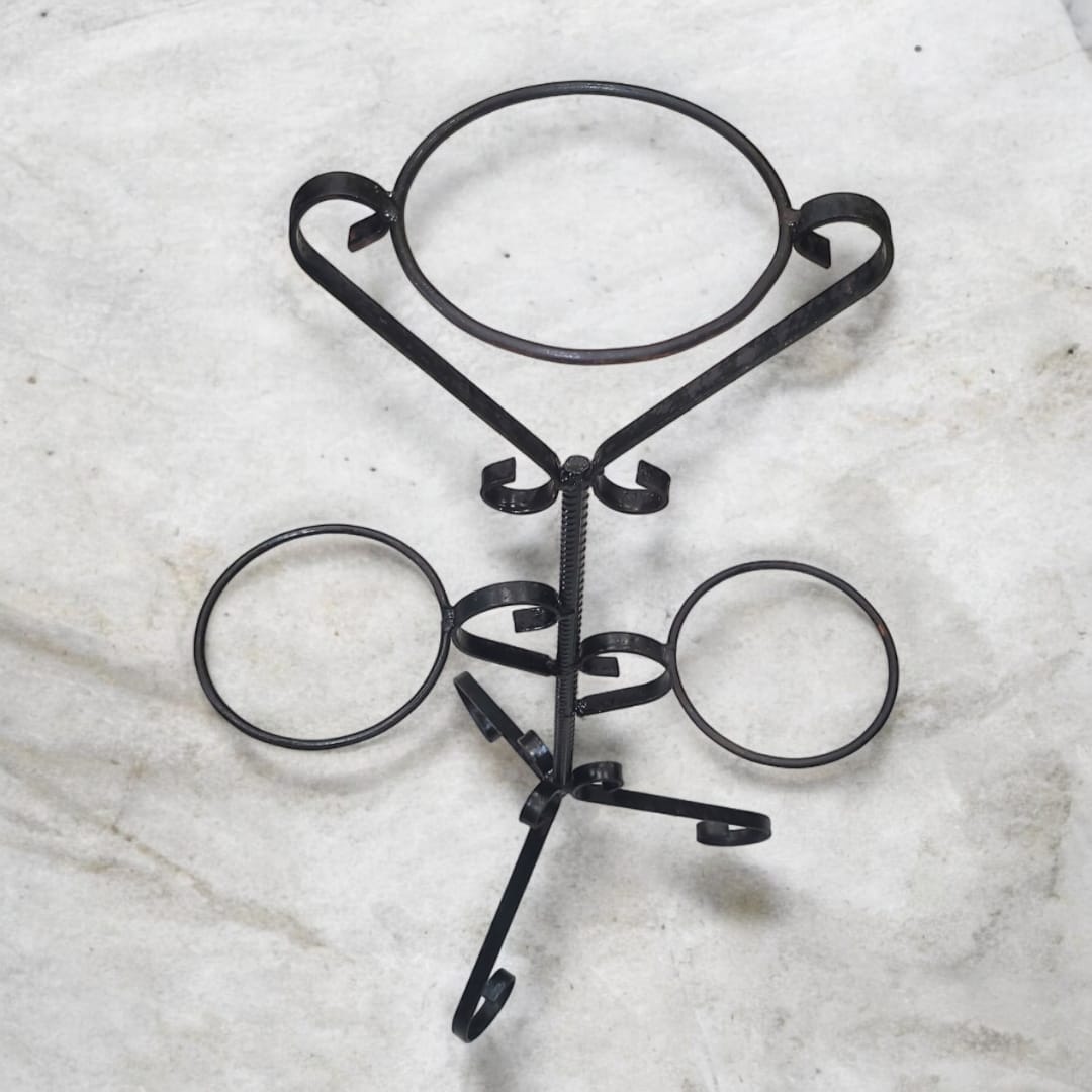 Vista frontal de macetero de hierro forjado con 3 soportes en color negro, diseño artesanal con detalles curvados y base estable.