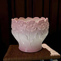 Macetero de porcelana con relieve floral en tonos rosados.
