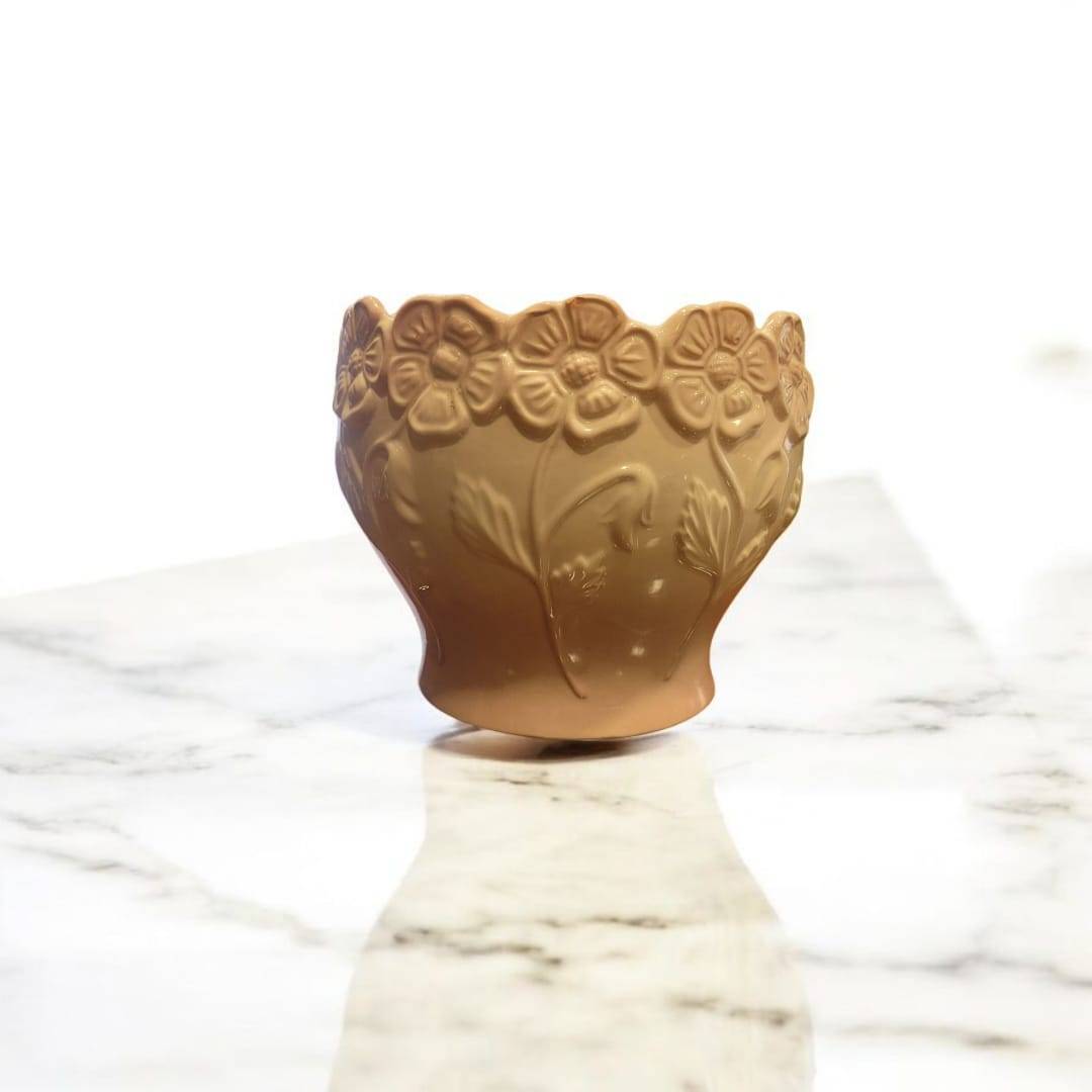 Maceta cerámica rosa esmaltada con relieve floral único sobre superficie de mármol, ideal para decoración de interiores o jardines con encanto.