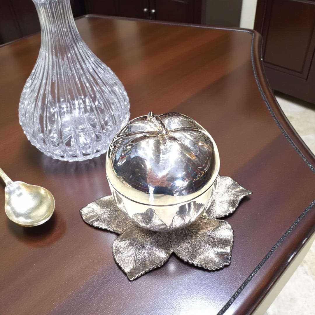 Azucarero de metal plateado con forma de manzana única y elegante sobre base de hojas decorativas, ideal para decoración de mesa distinguida.