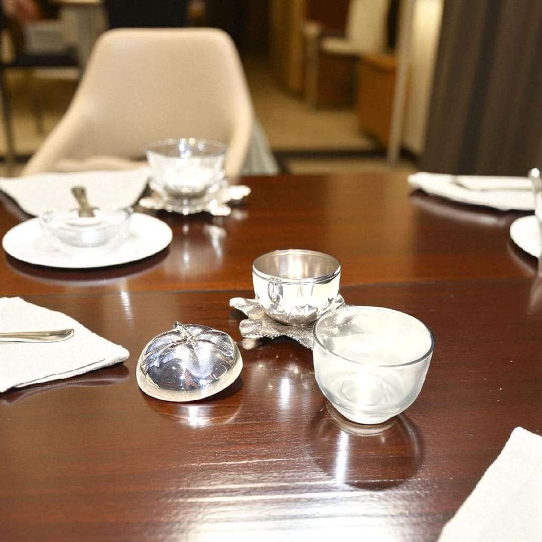 Azucarero de metal plateado con forma de manzana única y elegante sobre base de hojas decorativas, ideal para decoración de mesa distinguida.