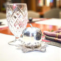 Azucarero de metal plateado con forma de manzana sobre base de hojas, junto a copa tallada, ideal para mesas refinadas y decoración exclusiva.