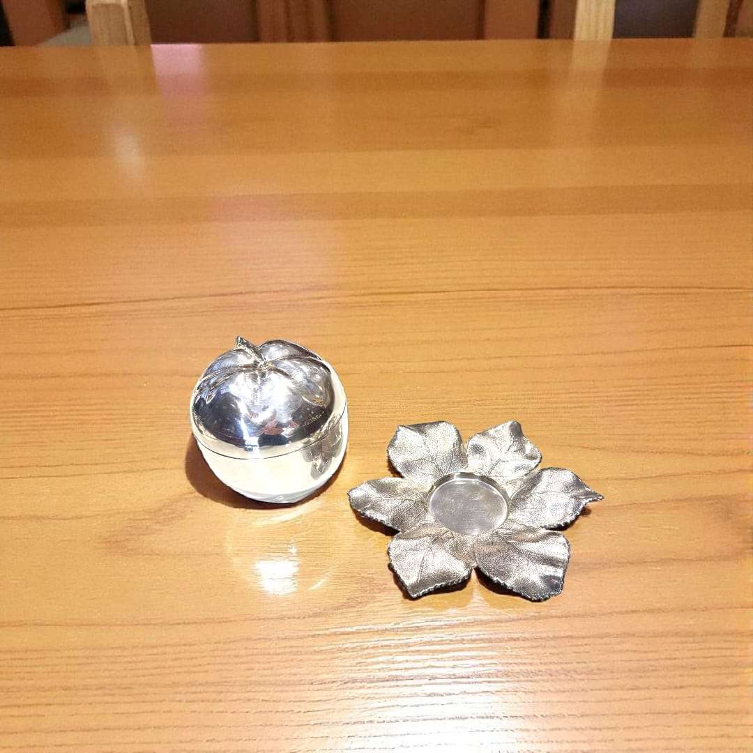 Azucarero de metal plateado con forma de manzana desmontado junto a base de hojas, ideal para decoración de cocina o comedor con estilo artesanal.
