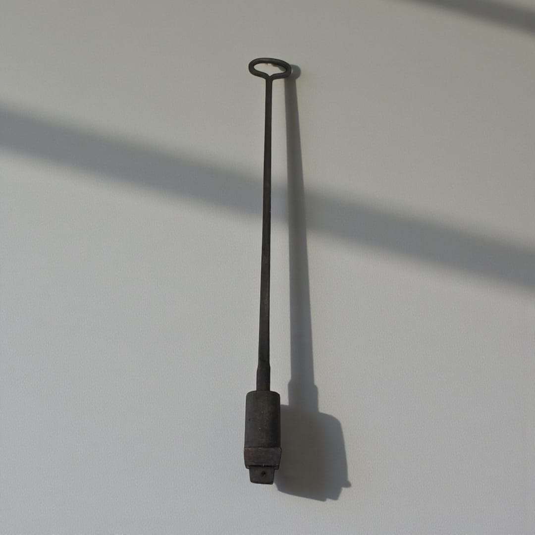 Marcador tonelero antiguo de forja con letra P, herramienta de hierro forjado colgada en pared blanca. Pieza única ideal para decoración rústica.