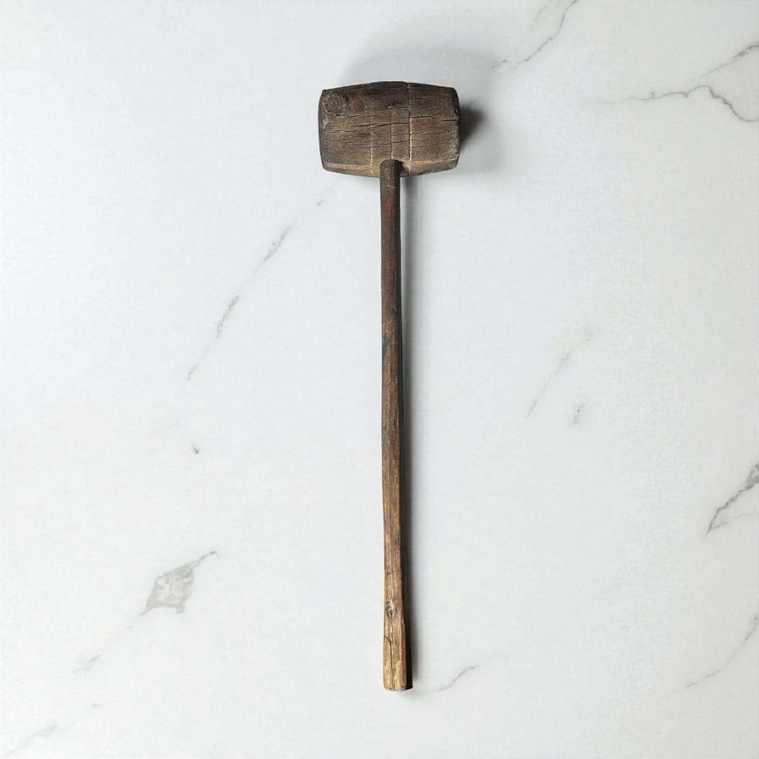 Mazo de madera antiguo visto en posición vertical sobre superficie clara.