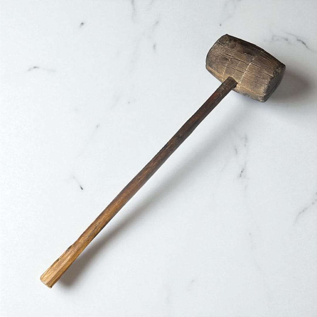 Mazo de madera antiguo visto en posición vertical sobre superficie clara.