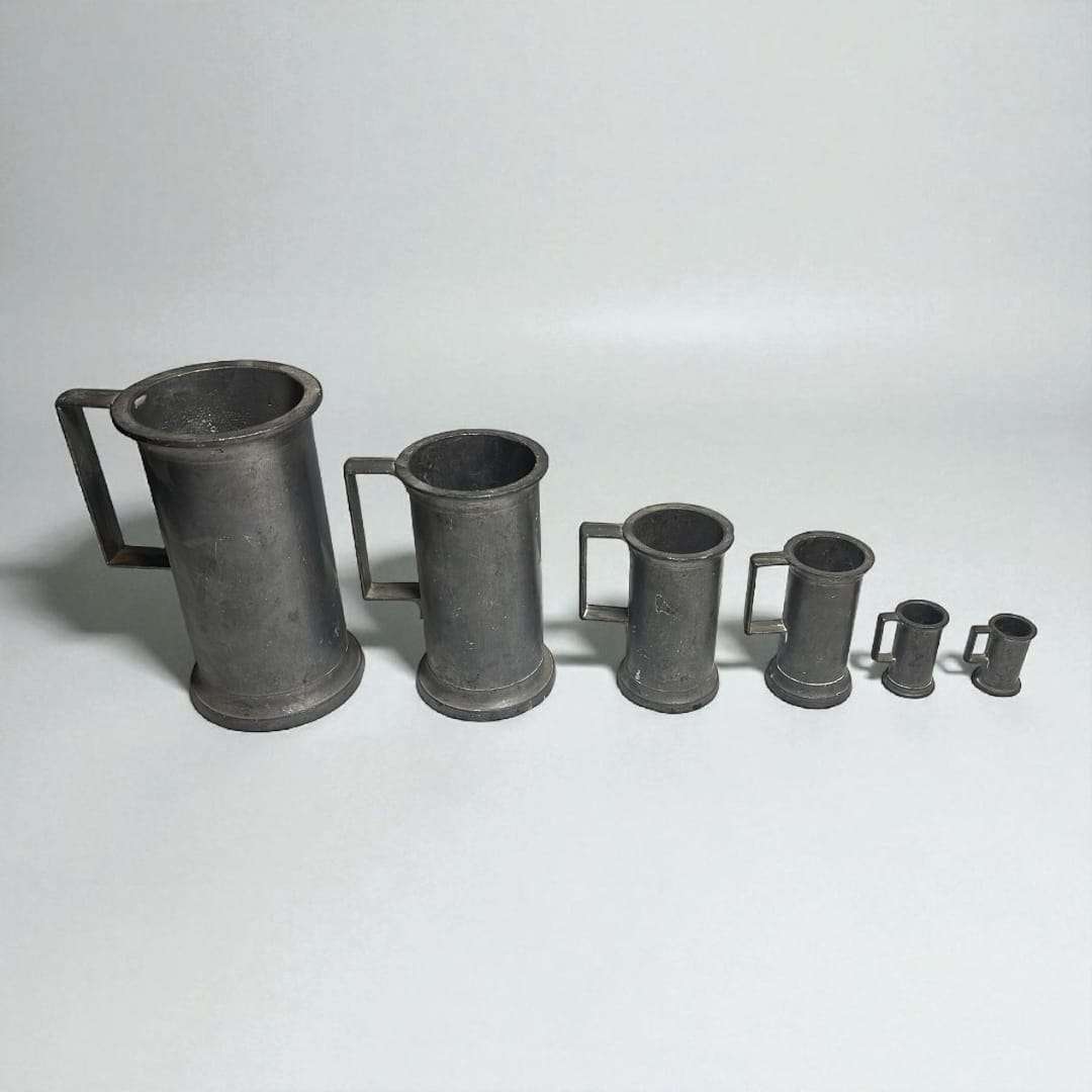 Conjunto completo de seis medidas de estaño vintage sobre fondo claro.