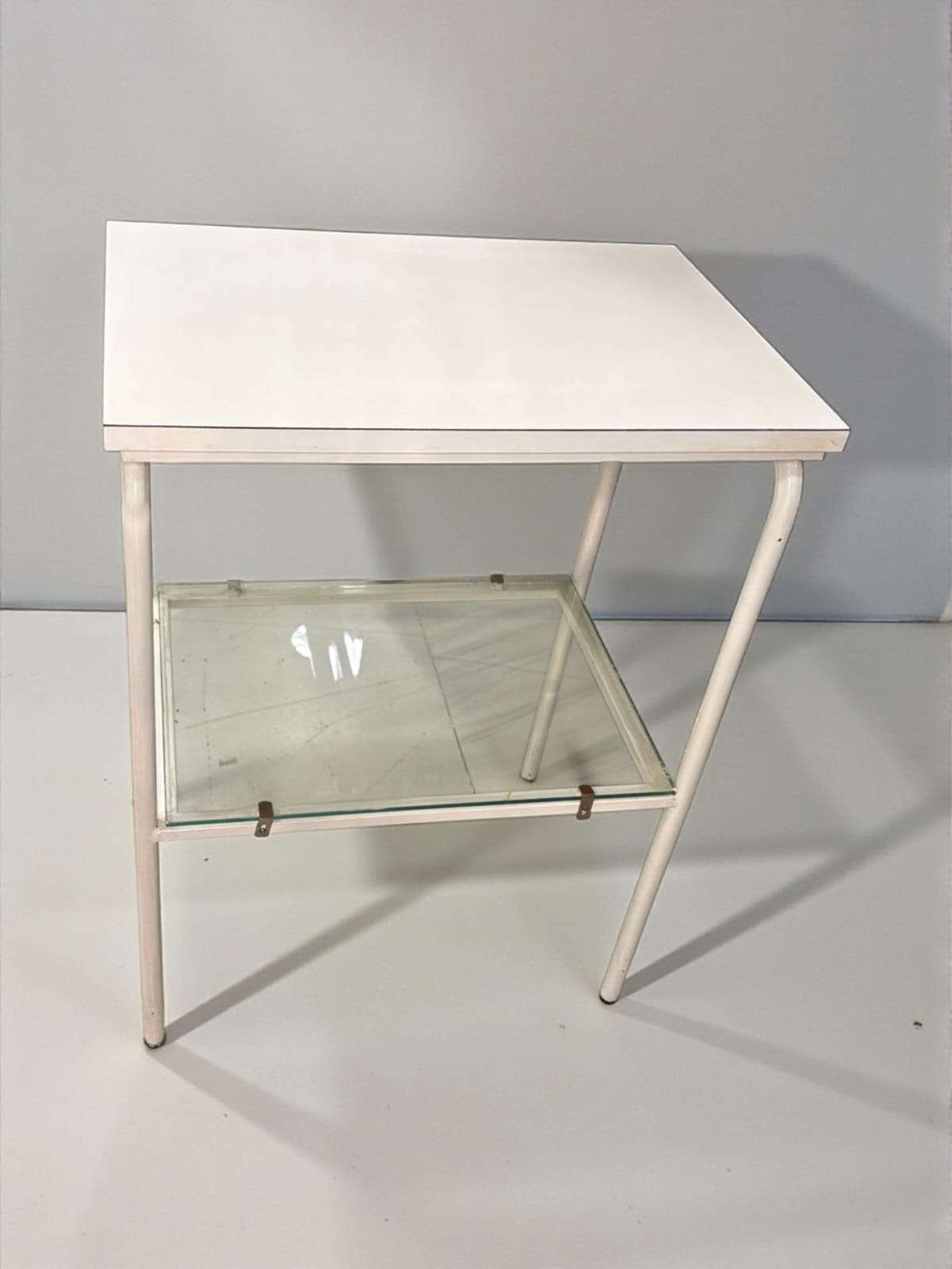 Mesa auxiliar blanca vintage con balda de cristal vista en ángulo frontal.
