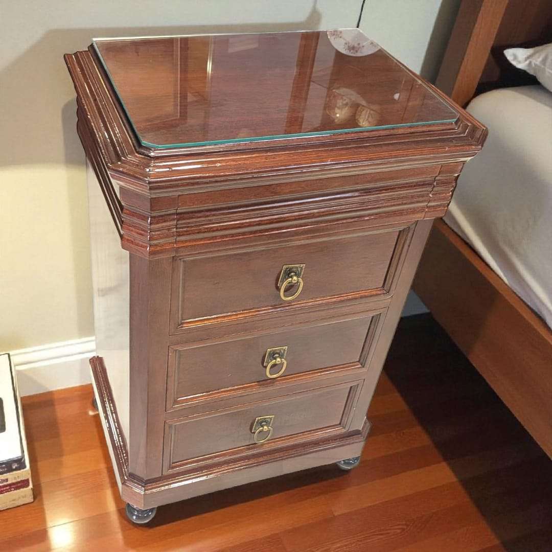 Mesitas de noche de caoba con tapa de cristal y cajón secreto, diseño clásico con tres cajones y tiradores metálicos dorados. Decoración elegante para dormitorio.