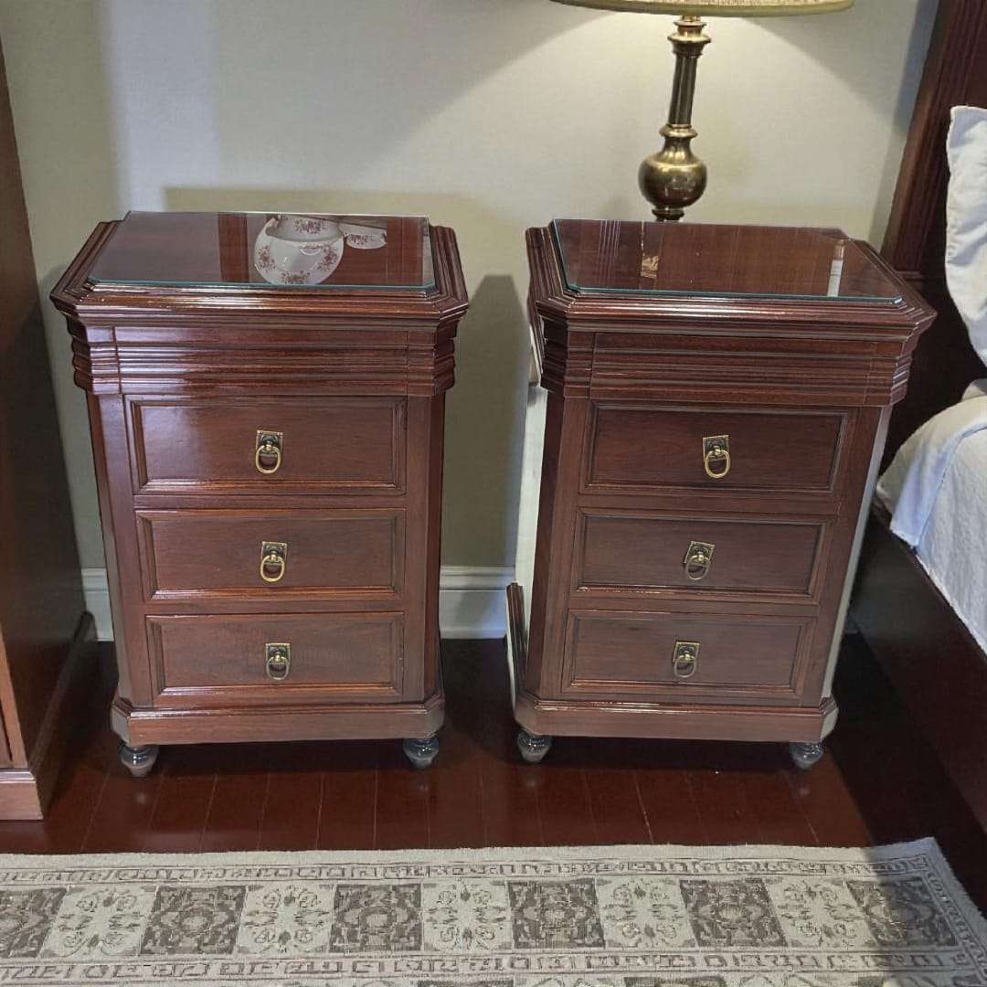 Mesitas de noche de caoba con tapa de cristal y cajón secreto, diseño clásico con tres cajones y tiradores metálicos dorados. Decoración elegante para dormitorio.