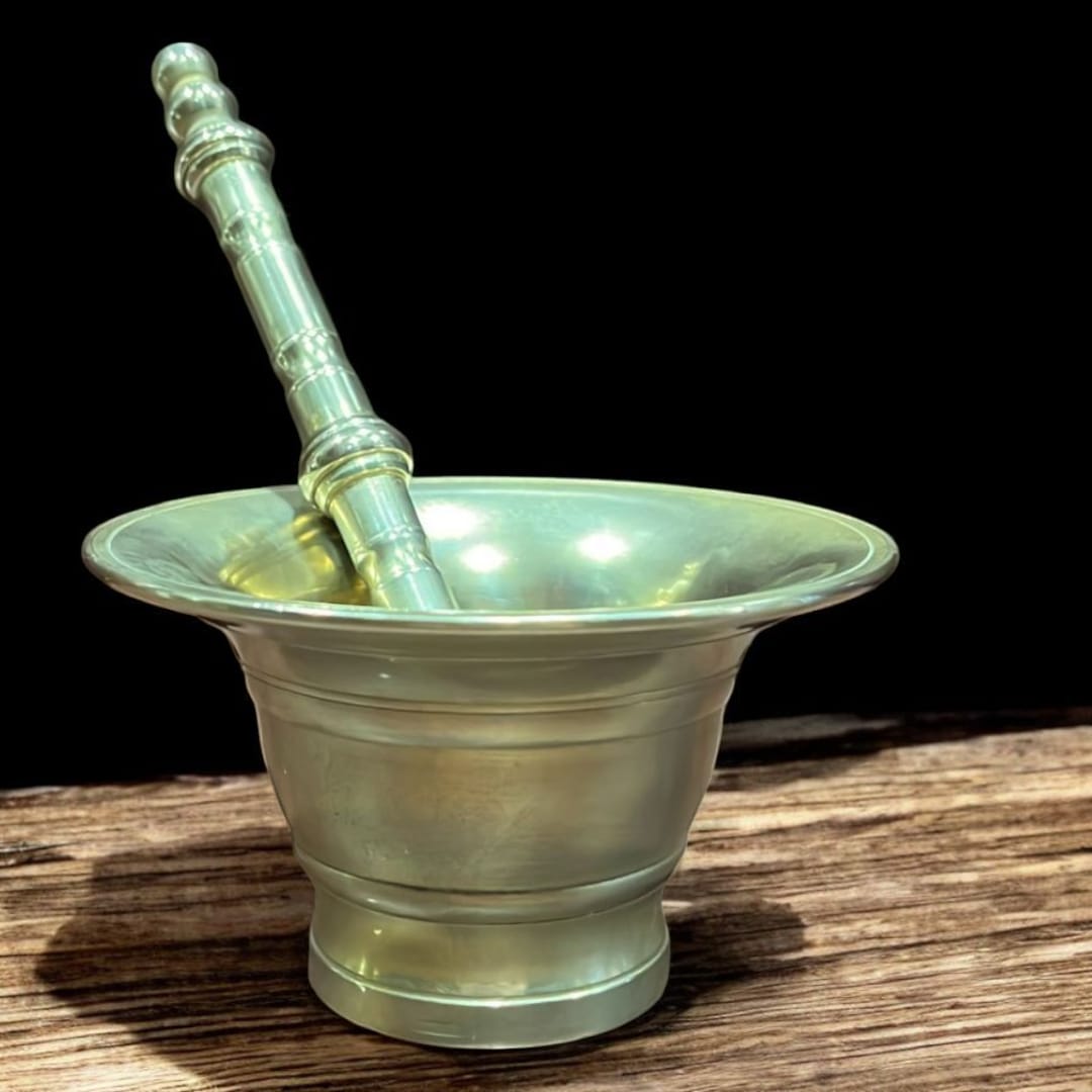 Mortero de bronce con maja antigua sobre superficie de madera, ideal para decoración vintage o cocina tradicional. Diseño único y calidad superior.