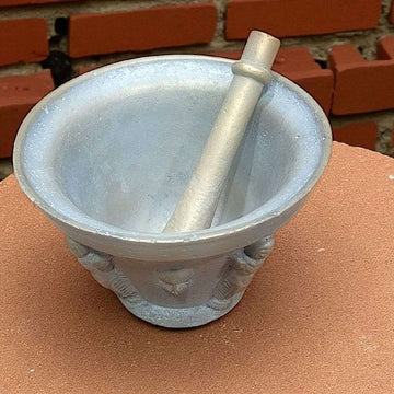 Mortero antiguo de bronce con relieves y maja única sobre superficie rústica. Ideal para decoración vintage en cocina o jardín.